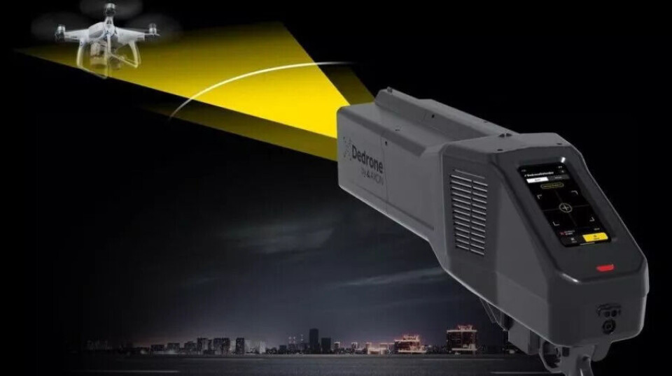 Illustrasjon fra selskapet Dedrone, som produserer jammeren DedroneDefender 2. Jammere er bærbare og batteridrevne. De kan rette jammingen mot dronene og forstyrre kontrollsystem og GPS-signaler. En håndholdt elektronisk enhet sender ut en gul stråle mot en flygende drone om natten med en opplyst byhorisont i bakgrunnen.