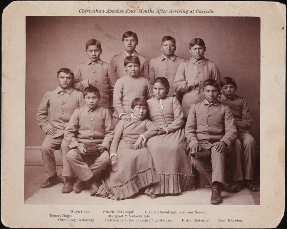 Bildet viser barn av Chiricahua Apache-stammen fire måneder etter at de kom til Carlisle Indian Industrial School i 1892. Den var drevet som en militærskole. Gruppebilde av elever i skoleuniform.