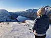 Person på snødekt fjell ser utover fjord og omkringliggende vinterfjell