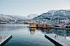 Snødekt havn i Tromsø med båter og fjell i bakgrunnen en vinterdag.
