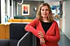Fotografi av Elin Vold Rutle, fagsjef i Forbrukerrådet. Kvinne med halvlangt hår, svart t-skjorte og rød cardigan lener seg på en skillevegg i et kontorlandskap.