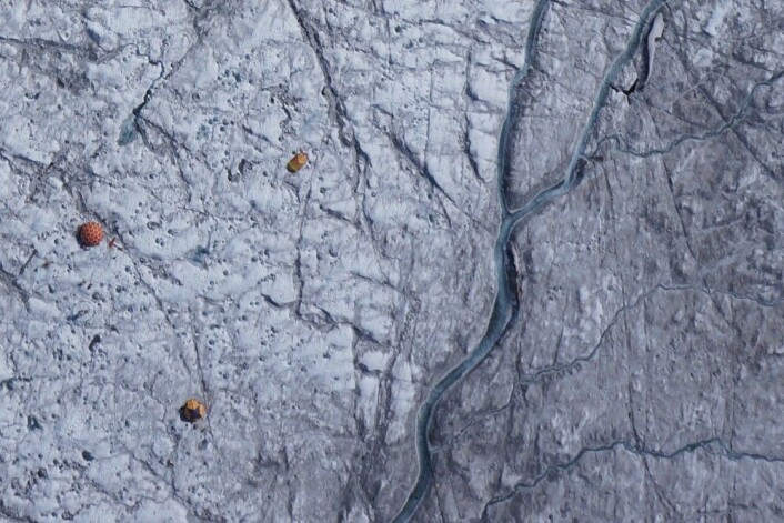 Dronebilde av teltene og det vitenskapelige utstyret på isen i Grønland. Den mørke isen, rik på urenheter, er særlig godt synlig øst for smelte-elven nært leiren. (Foto: J.Ryan / J.Box / A.Hubbard) Dronebilde av teltene og det vitenskapelige utstyret på isen i Grønland. Den mørke isen, rik på urenheter, er særlig godt synlig øst for smelte-elven nært leiren. (Foto: J.Ryan / J.Box / A.Hubbard)