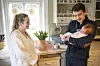 Foreldre står på et lyst kjøkken mens far holder en nyfødt baby i armene