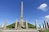 Høyt steinmonument på gresshaug omgitt av mindre steinstøtter