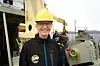 Person med gul hjelm på forskningsfartøy, med utstyr og sjø i bakgrunnen.