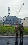 To personer står foran den innkapslede reaktoren i Tsjornobyl med en kran i bakgrunnen.