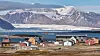 Ny-Ålesunds bygninger foran fjord og store isbredekte fjell på Svalbard.