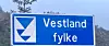 Blått Vestland fylke-skilt med våpen foran åsside i bakgrunnen