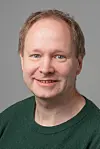 Portrett av voksen person i grønn genser mot nøytral grå bakgrunn.