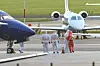 Helsearbeidere i beskyttelsesutstyr på en flyplass. To fly.