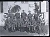 En gruppe soldater i uniform poserer foran en bygning med skodder og et veggskilt.