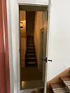 Åpen dør inn til en smal gang med trapp og varmt lys i et innendørs rom.