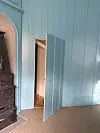 Lyseblått rom med åpen dør, svart ovn til venstre og teppebelagt gulv.