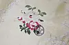 Brodert blomstermotiv i rosa, rødt og grønt på lyst stoff med svart stempel.
