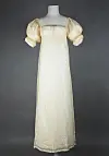 Lys lang kjole med korte puffede ermer på en mannequin mot mørk bakgrunn.