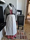 En historisk drakt står utstilt ved en svart vedovn i Eidsvollsbygningen, der historien om husholdersken Elise Harward trekkes fram.