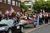 Parade med folk i tradisjonelle klær, amerikanske og norske flagg, samt en dekorert båt på henger.