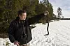 Mann holder opp en hoggorm over snø i et skogsområde.