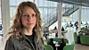 Kvinne i forgrunnen i et lyst kontorlandskap med trapper og grønne stoler.