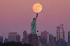 Stor supermåne over Frihetsgudinnen med Brooklyn-bybildet i bakgrunnen ved skumring.