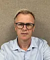 Mann med briller og lyseblå skjorte foran en nøytral bakgrunn.