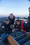 Frode Kvalø, Espen Saastad, Erik Erland Holmen inspiserer gjenstandene de har hentet opp fra havets bunn ombord på et skip i nydelig solnedgang.