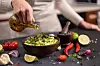 Hånd heller olivenolje i en bolle med salsa ved siden av lime, chili og tomater.