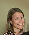 Nært portrett av en smilende kvinne foran en lys, nøytral bakgrunn.