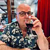 Portrettbilde av professor Arve Hjelseth med blomstrete skjorte og et glass vin som han holder opp til munnen.