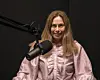 En kvinne sitter foran en mikrofon i et podkaststudio med mørk bakgrunn.