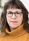 Nærportrett av kvinne med briller og brun høyhalset genser mot lys bakgrunn.
