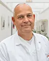 Portrettbilde av kreftlege Tormod Kyrre Guren, i hvit legefrakk. I bakgrunnen skimtes en sykehuskorridor.