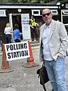 Et valglokale med skiltet «POLLING STATION», to politibetjenter og flere personer foran en bygning.