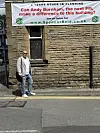 En mann står ved siden av en murbygning med et stort banner som oppfordrer Andy Burnham til å redde bygget.