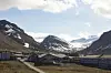 Utsikt over en dal med bygninger i forgrunnen, snødekte fjell og delvis skyet himmel.