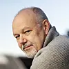 Nærbilde av en eldre mann med kort grått hår og skjegg i grå genser.