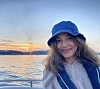 Portrettbilde av en smilende Hijab Fatima Ali. Hun er på en båt og har på seg en flytevest, og en båthatt i olastoff på hodet. I bakgrunnen ser vi havet og en solnedgang.