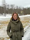 En kvinne i grønn vinterjakke står utendørs foran snø og bare trær.