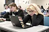 Elever sitter ved pulter med bærbare PC-er i et klasserom og ser slitne ut.