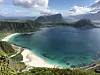 Utsikt over en turkis lagune med hvite strand omringet av fjell.