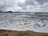 Sandstrand med lave bølger under en overskyet himmel.