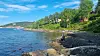 Steinete strand ved havet med tre personer som går nær vannkanten og grønne trær langs kysten.