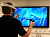 En person med VR-briller står foran en TV og holder to håndkontrollere.