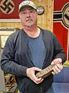 Steinar Grønnås står innendørs og holder en rusten metallbit fra Tirpitz.