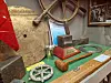 Historisk maritim utstilling med skipratt, tau, metallgjenstander og modeller på et grønt bord.