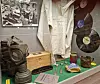 Utstillingsmontre med hvit drakt, antikke gjenstander, kamera og stor vinylplate.
