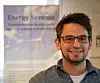En mann med briller står foran en plakat med teksten Energy Systems og et bilde av vindturbiner.