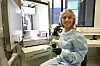 En person i beskyttelsesklær sitter ved en laboratoriemaskin og holder et kretskort i et lyst arbeidsrom.