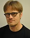 Portrett av Henrik Glenner med briller foran en lys, nøytral bakgrunn.