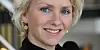 Nærbilde av en smilende kvinne med blondt hår og gullfargede øredobber.